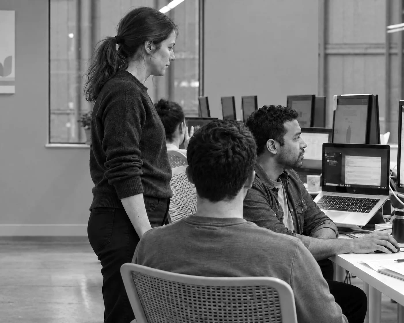 Een docent staat bij drie collega's aan hun laptops