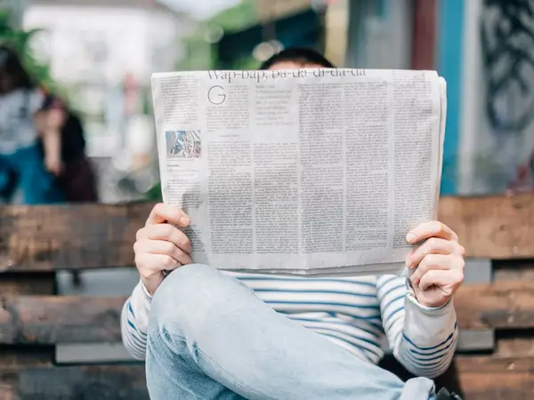 Iemand op een bankje leest een krant.